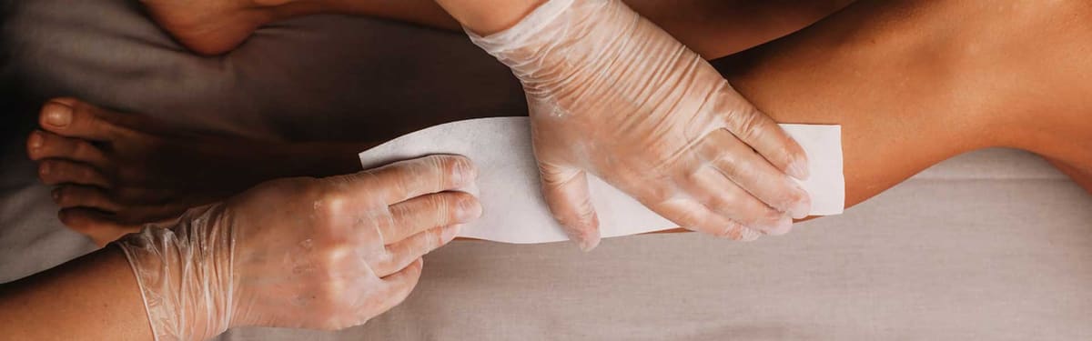 Benen worden met een harsstrook onthaard door een schoonheidsspecialiste met handschoenen