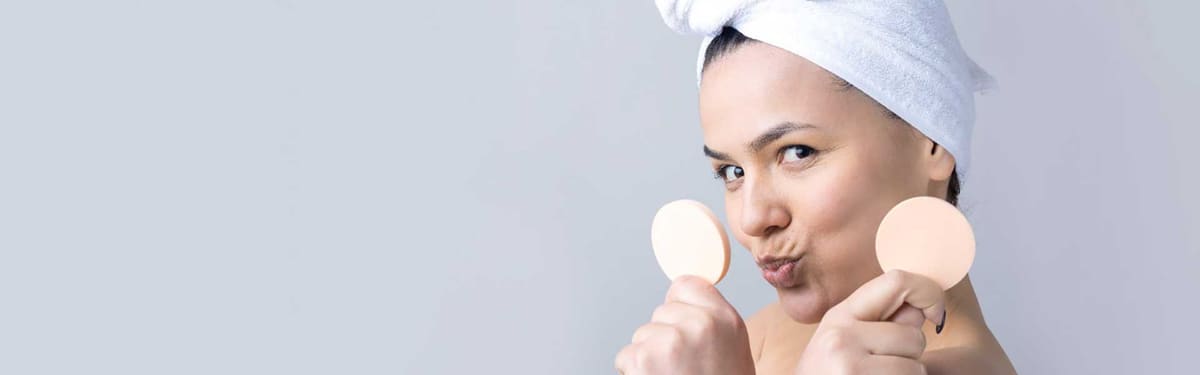 Woman in a bath towel holding two make-up removal sponges before a facial
